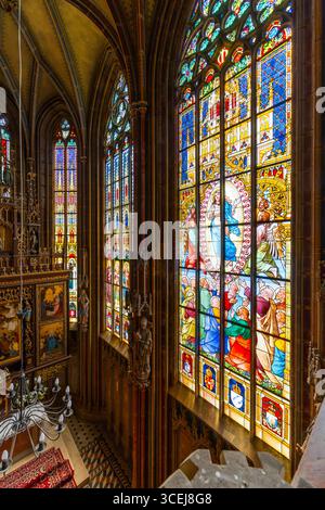 Sonnenlicht, das durch lebendige Buntglasfenster strahlt, zeigt religiöse Szenen in einer Kirche und schafft eine spirituelle Atmosphäre Stockfoto