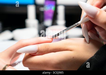 Professionelle Maniküre tragen bei der Nagelverlängerung sorgfältig gellack auf, um eine perfekte, gleichmäßige Abdeckung und Form zu gewährleisten. Stockfoto