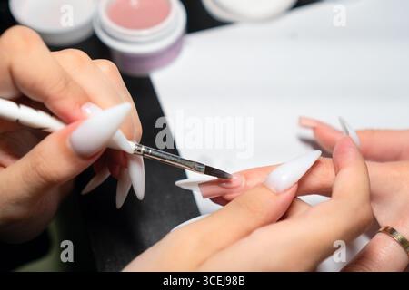 Professionelle Maniküre tragen bei der Nagelverlängerung sorgfältig gellack auf, um eine perfekte, gleichmäßige Abdeckung und Form zu gewährleisten. Stockfoto