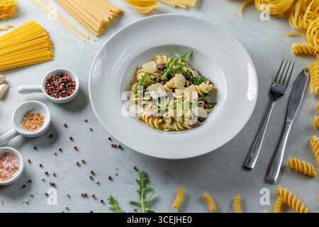 Köstliche Fusilli-Pasta mit Parmesan, Rucola und Hackfleisch serviert auf weißem Teller, umgeben von verschiedenen Zutaten Stockfoto