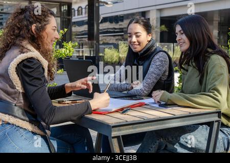 Drei Universitätsstudenten arbeiten an einem Projekt zusammen, verwenden einen Laptop und machen sich im Freien Notizen Stockfoto