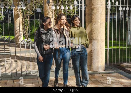 Drei junge Frauen spazieren gemütlich durch einen Park, unterhalten sich und genießen die Gesellschaft der anderen Stockfoto