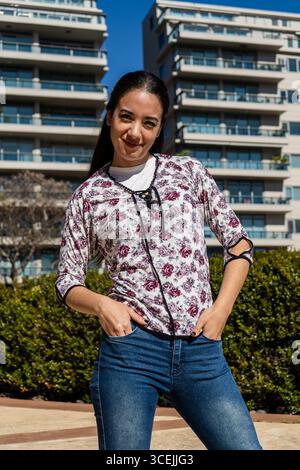 Selbstbewusste junge Frau, die mit Händen in Taschen vor modernen Wohngebäuden steht und den urbanen Lebensstil genießt Stockfoto