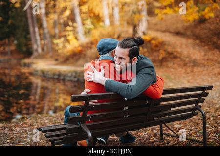 Grandad und Enkel sitzen auf einer Bank im Park und umarmen sich. Stockfoto