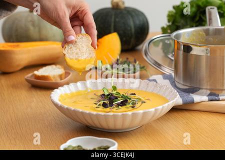 Brot von Hand in Gemüsesuppe mit Mikrogrün und Kürbis auf dem Tisch tauchen Stockfoto