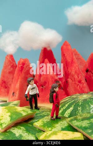 Miniaturgänger, die mit Rucksäcken auf Wassermelonenbergen wandern. Stockfoto