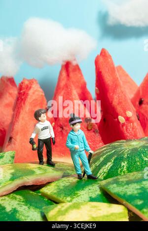 Miniaturgänger, die mit Rucksäcken auf Wassermelonenbergen wandern. Stockfoto