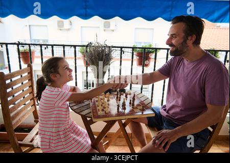 Ein Vater und eine Tochter teilen sich einen freudigen Moment beim Schach auf ihrem Balkon und zeigen ihre Verbundenheit durch Spaß und Spiele. Die Einstellung erzeugt ein warmes und h Stockfoto