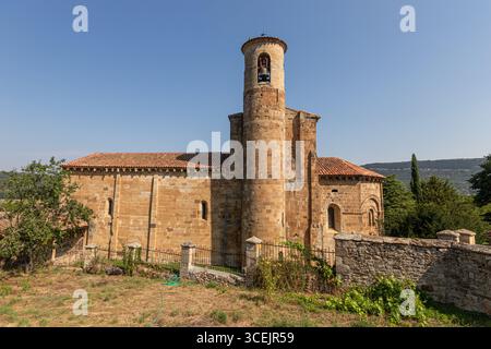Valderredible, Spanien. Seitenansicht der romanischen Stiftskirche San Martin de Elines mit ihrem zylindrischen Glockenturm, Quirlenmauerwerk und einem Mais Stockfoto