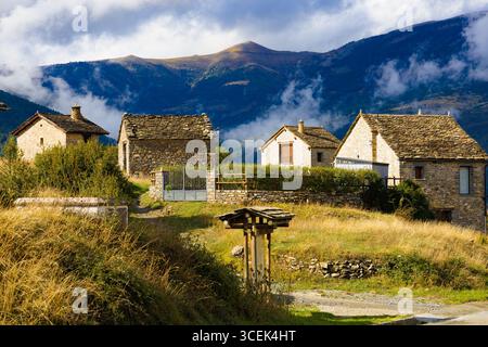 Bezaubernde Steinhäuser im kleinen Bergdorf Nerin, beleuchtet von goldenem Sonnenlicht, mit nebeligen Hügeln in Ordesa, Aragon, Spanien. Stockfoto