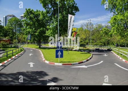 Go-Kart-Strecke im Freien, umgeben von üppig grünen Bäumen und Gras, mit klaren Straßenmarkierungen, Verkehrsschildern und bunten Fahnen, unter einem hellblauen Himmel Stockfoto