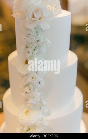 Eine atemberaubende dreistöckige Hochzeitstorte mit weißen Blumen sorgt für die festliche Atmosphäre der Veranstaltung. Stockfoto
