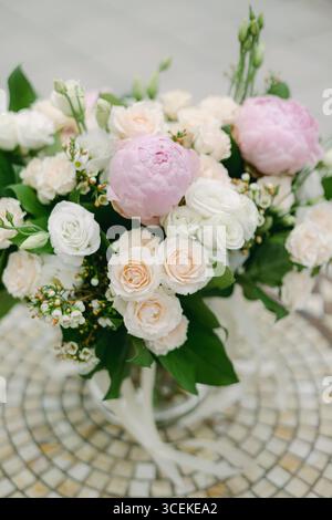 Wunderschöner Blumenstrauß aus eleganten Pfingstrosen und zarten Rosen, die auf einer dekorativen Fliesenoberfläche angeordnet sind. Stockfoto