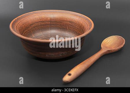 Tonschale mit Holzlöffel isoliert auf schwarzem Hintergrund Stockfoto