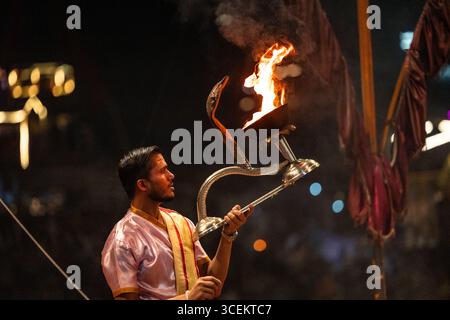 Ein hinduistischer Priester, der während der Ganga aarti Zeremonie in Varanasi, Indien, einen brennenden aarti hält, zeigt eine lebendige Darstellung der Hingabe und Spiritualität in A Stockfoto
