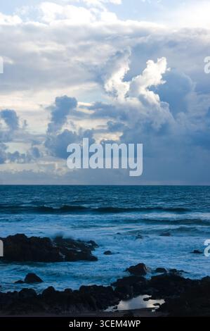 Eine malerische Aussicht auf das Meer mit Wellen, die unter einem bewölkten Himmel gegen die Felsen krachen. Stockfoto