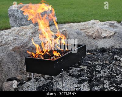 Tragbarer Grill mit Feuerbrand im Freien von Stone. Ein tragbarer rechteckiger Grill, der ein Feuer mit Flammen aufhält. Der Grill wird platziert Stockfoto