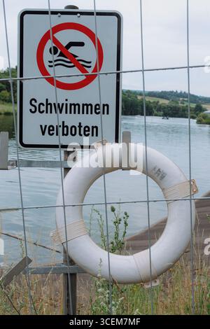 Kein Badeschild mit Sicherheitsring am Fluss, was die Vorsicht betont. Das Schild verbietet Schwimmen, um die Sicherheit in der Nähe des Wassers zu gewährleisten. Vegetation umgeben Stockfoto
