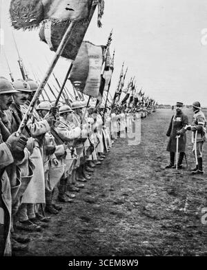 Mai 1916, erster Weltkrieg: General Gouraud inspiziert eine große Parade von Regimentsflaggen, um eine französische Division zu ehren, die in Verdun ausgezeichnet wurde. Soldaten stehen in Formation mit Gewehren und Bannern, die Opfer und Nationalstolz symbolisieren. Diese feierliche Übersicht, die am 6. Mai 1916 in LíIllustration veröffentlicht wurde, spiegelt die Bedeutung von Verdun als Symbol der französischen Ausdauer während des Ersten Weltkriegs und die Rolle militärischer Traditionen für Moral und Erinnerung wider. Stockfoto