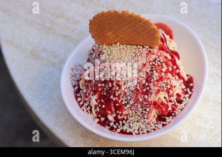Traditionelles deutsches Spaghettieis Dessert aus Vanilleeis, das in spaghettiähnliche Fäden gepresst und mit Erdbeersauce garniert und gerieben wird Stockfoto