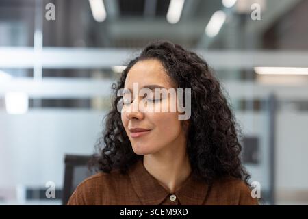 Porträt einer ruhigen Frau, die mit geschlossenen Augen lächelt und in einem Büro steht. Sie erscheint in Ruhe und genießt während ihres Tages einen beruhigenden Moment an einem professionellen Arbeitsplatz. Stockfoto