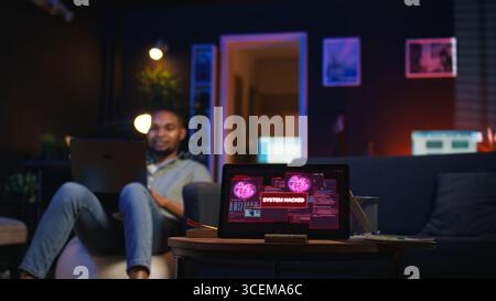 Black IT Professional in Loft arbeitet an Cybersicherheit mit Gadgets, geht Hacking-Versuchen, Verschlüsselung und Cyberabwehr an. Der Bildschirm zeigt Warnungen zu Sicherheitsverletzungen und Datensicherheitsrisiken an. Kamera A.. Stockfoto
