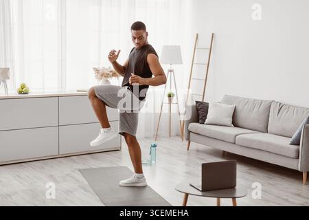African Guy Tun Stehende Knie Erhöhen Übung Bei Laptop Indoor Stockfoto