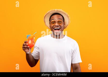 Überfröhlicher schwarzer Mann in legerer Kleidung mit erfrischendem Sommercocktail, der den Mund vor Aufregung auf gelbem Hintergrund öffnet Stockfoto