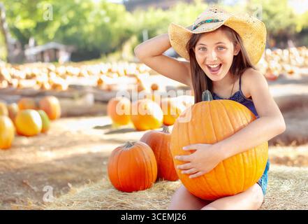 Hübsches Mädchen mit Cowboy-Hut, das den Kürbis-Patch an einem sonnigen Herbsttag genießt. Stockfoto