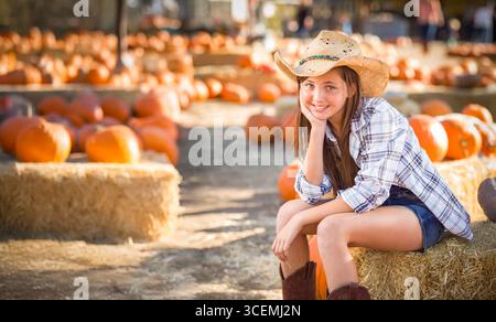 Hübsches Mädchen mit Cowboy-Hut, das den Kürbis-Patch an einem sonnigen Herbsttag genießt. Stockfoto