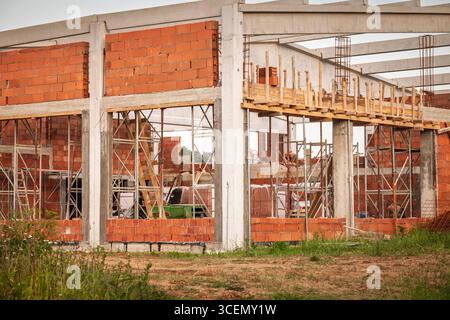 Der Bau eines neuen Lagers an einem großen Standort mit Betonsäulen, gemauerter Füllung, Gerüsten und Stahlträgern wird vorangetrieben. Der Rahmen markiert die Schächte für einen Stockfoto