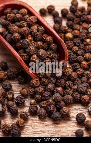 Ganze schwarze Pfefferkörner in Holzlöffel auf verwitterter Holzoberfläche Stockfoto