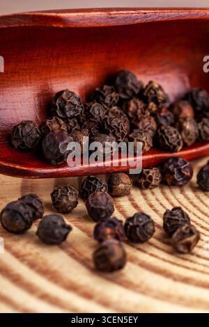 Ganze schwarze Pfefferkörner in poliertem Holzlöffel auf Matte Stockfoto