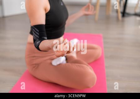 Die Beine von Frauen werden in Lotusform auf einer rosafarbenen Yogamatte gekreuzt, wodurch die Haltung, das Stretching und die Flexibilität im Innenbereich hervorgehoben werden Stockfoto