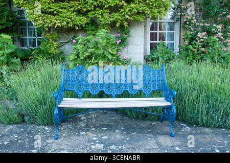 Die hellblaue Bank befindet sich inmitten von lebendigem Grün neben einer bezaubernden Steinstruktur und schafft eine friedliche Gartenatmosphäre. Stockfoto