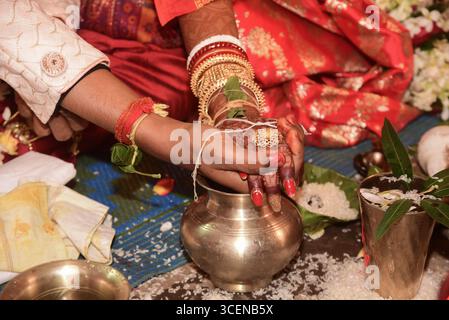 Nahaufnahme einer hinduistischen Hochzeitszeremonie, die die Hände der Braut und des Bräutigams in einem heiligen Ritual zeigt, verziert mit traditionellem Schmuck und roter Kleidung Stockfoto
