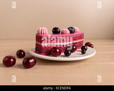 Appetitliches Stück Kirsch- und Heidelbeerkuchen mit rosa Zuckerguss, garniert mit Schlagsahne und frischen Beeren, präsentiert auf einem weißen Teller Agave Stockfoto