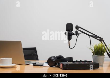 Podcast Studio-Einrichtung mit professionellem Mikrofon am Arm, Laptop, Kopfhörer, Audiomischer, Smartphone, Kaffeetasse auf Holzschreibtisch, repräsentiert di Stockfoto