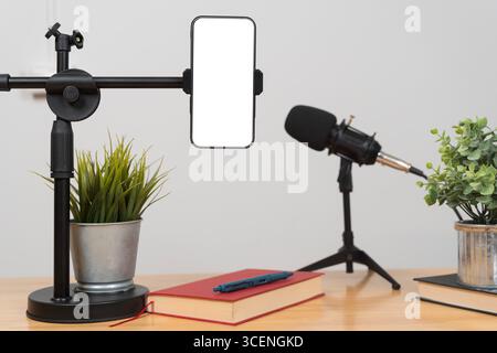 Minimalistisches Podcast-Studio-Setup mit professionellem Mikrofon, Smartphone-Halter, Büchern und dekorativen grünen Pflanzen auf einem Holztisch für mehr Mo Stockfoto