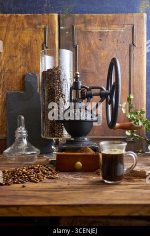 Rustikale Kaffeeszene mit Vintage-Mahlwerk, gerösteten Bohnen, gemahlenem Kaffee, Croissants und Grün auf einem Holztisch. Gemütliches Farmhouse-Frühstück im Stil Stockfoto