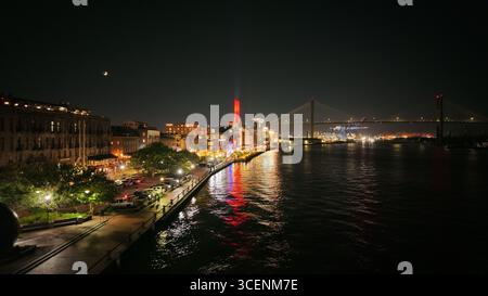 Blick aus der Vogelperspektive auf den Savannah River, der die pulsierenden Lichter der Stadt reflektiert, mit der Talmadge Memorial Bridge in der Ferne, Savannah, Georgia, USA. Stockfoto