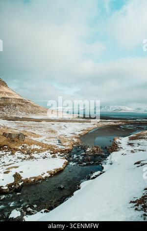 Kirkjufell-Berg mit einem Bach, der durch Schnee fließt, Kirkjufellsfoss, Kirkjufell, Grundarfjörður, Island Stockfoto