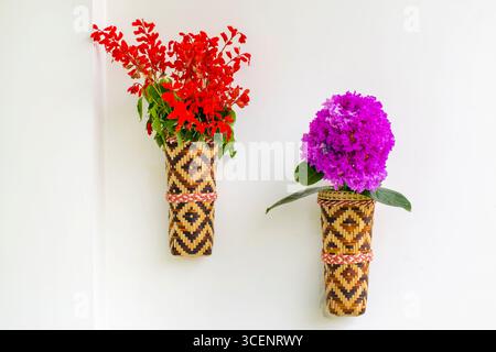 Bambusblumenvase mit roten Fliederblüten, die an der weißen Wand hängen. Isolierter Hintergrund. Stockfoto