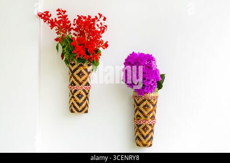 Bambusblumenvase mit roten Fliederblüten, die an der weißen Wand hängen. Isolierter Hintergrund. Stockfoto
