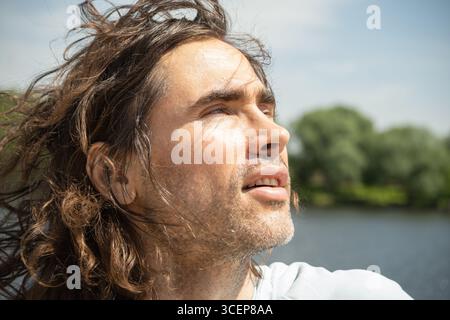 Fröhlicher Brünette Mann genießen und in die Sonne schauen im Stadtpark. Genießen Sie die Natur und den sonnigen Tag. Sommer. Reflexion und Fernweh. Atmen Sie saubere Luft ein Stockfoto