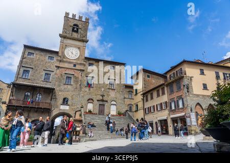 Cortona, Toskana, Italien - 24. April 2025: Blick auf die Piazza della Repubblica, wo warme Steinbauten den belebten Platz umgeben, während die Menschen sich unter einem hellen, weiten Himmel versammeln. Stockfoto