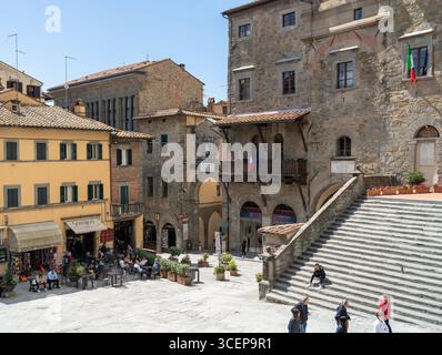 Cortona, Toskana, Italien - 24. April 2025: Blick auf die Piazza Della Repubblica, wo alte Steinhäuser und verwitterte Treppen unter einem hellen s aufeinander treffen Stockfoto
