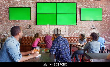 Leute, Die An Tischen In Der Sports Bar Sitzen Und Sich Das Spiel Auf Grünen Bildschirmen Ansehen Stockfoto