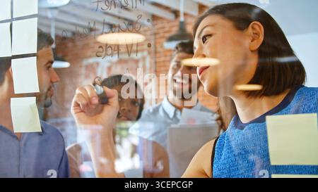 Geschäftsfrau schreiben Ideen auf Glasscheibe während der Sitzung Stockfoto