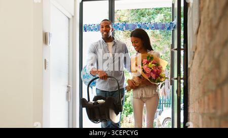 Eltern Mit Blumen Kommen Mit Neugeborenem Baby Im Kindersitz Nach Hause Stockfoto